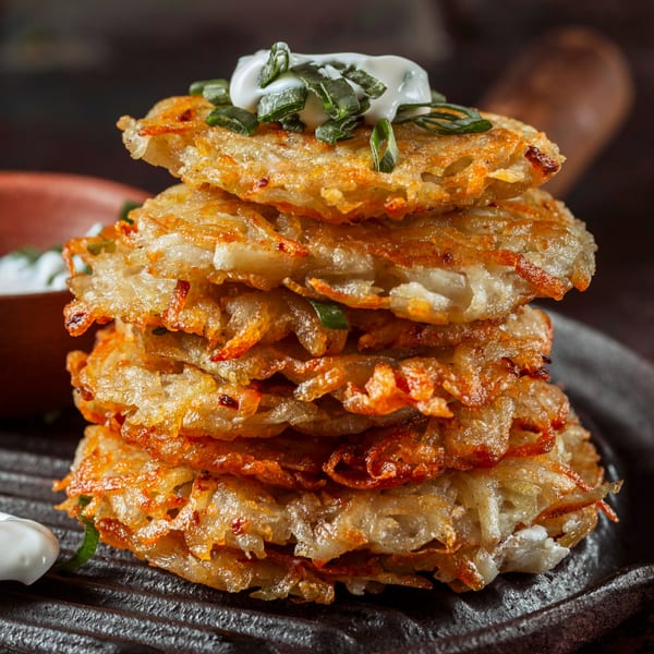 A stack of crispy golden-brown hash browns topped with sour cream and chopped green onions.
