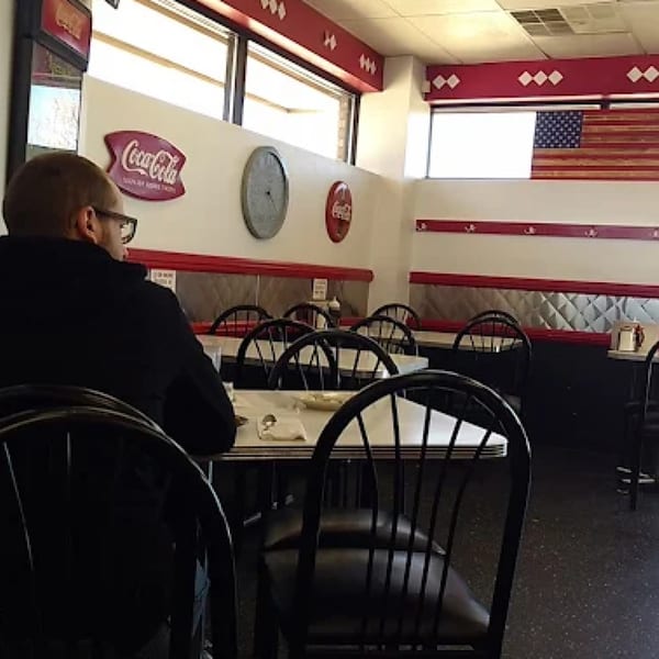 A man sits at a table in Ted's Coney Island diner with retro decor and an American flag.