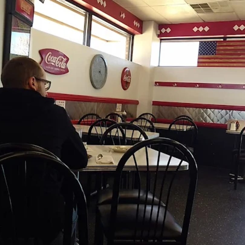 A man sits at a table in Ted's Coney Island diner with retro decor and an American flag.