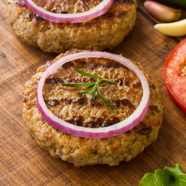 Two grilled burger patties topped with red onion slices and a sprig of rosemary on a wooden board.
