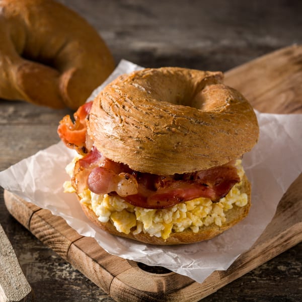 A bagel sandwich with scrambled eggs and bacon on a wooden cutting board at Ted's Coney Island.